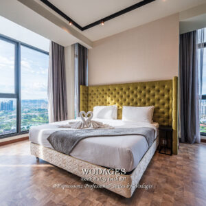 A modern apartment bedroom featuring a dressed bed with a green tufted headboard, hardwood flooring, and floor-to-ceiling windows.